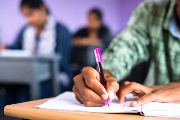 close up shot of college student writing notes on book at classroom concept of